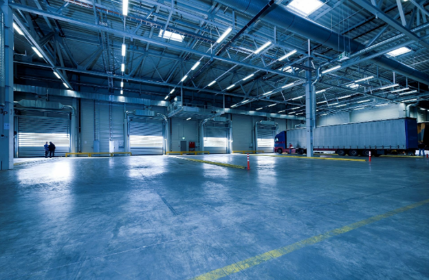 Empty warehouse interior with roller shutter dock doors, yellow floor markings and a parked trailer