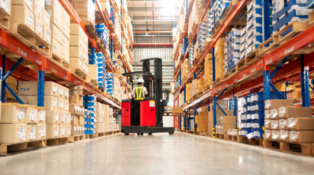 Worker on a red reach truck in a warehouse aisle between tall racking stacked with cartons