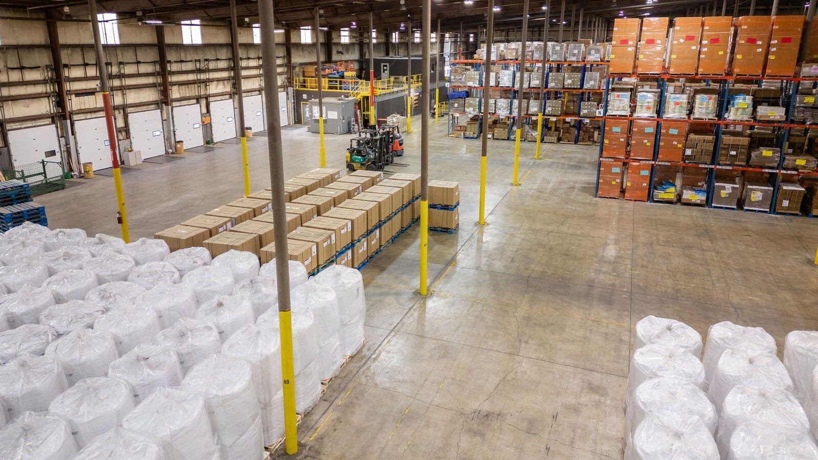 Warehouse floor with dock doors, forklift, palletized cartons, and bulk bags