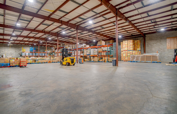 Yellow forklift on the open concrete floor of a steel-framed warehouse lined with pallet racking