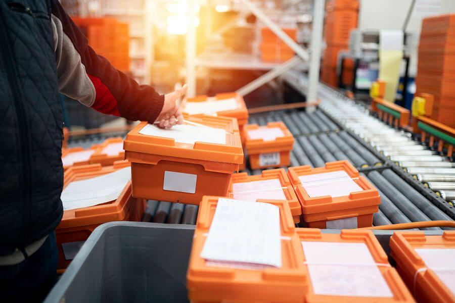 Worker sorting orange bins on a conveyor during pick and pack fulfillment